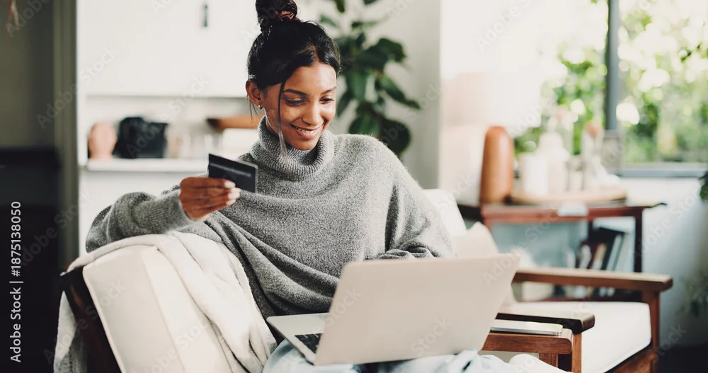 Woman sitting on a couch using a laptop while holding a credit card