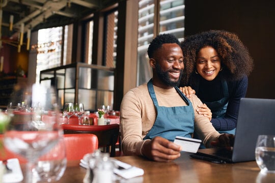 Restaurant owners using a laptop while one holds a payment card to finalize a transaction