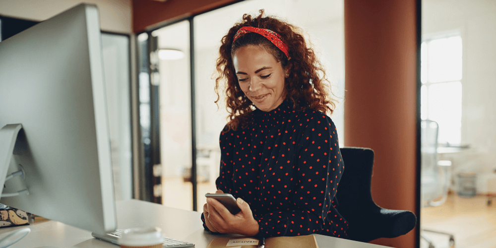 woman using mobile phone to enroll in Easy Save at desk with computer