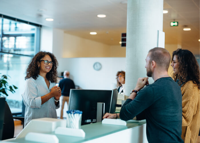 Two customers speaking with a staff member and receiving friendly assistance at a public service reception desk