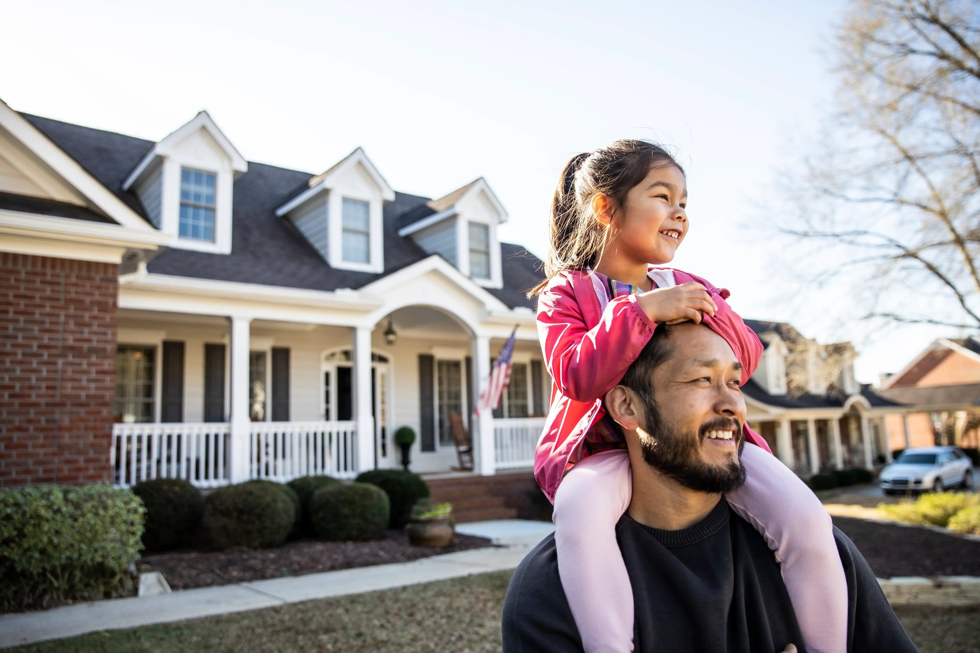 Father carrying his daughter on his shoulders while spending time together outside their home
