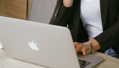Person working on a laptop at a desk, typing on a keyboard while wearing a blazer