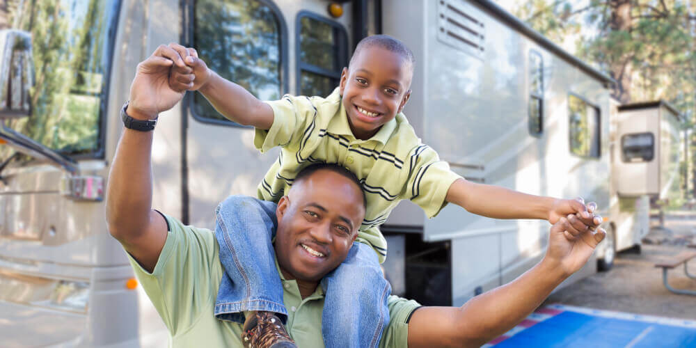 Man with child on his shoulders in front of an RV