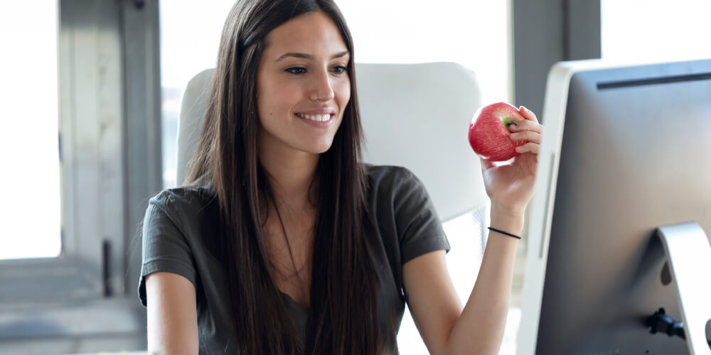 woman holding an apple looking at the computer