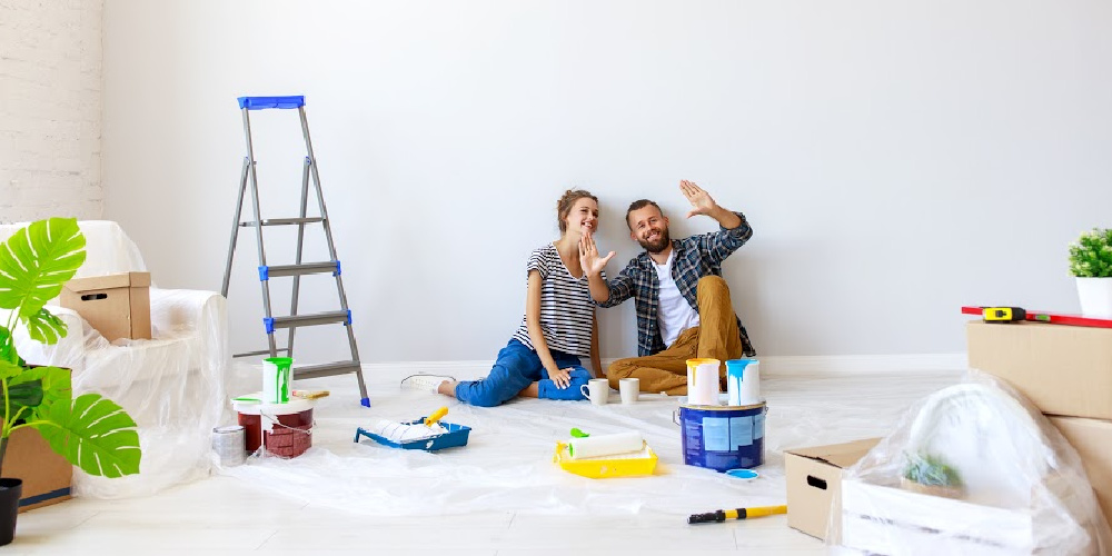 Couple in living room with paint, ladders and paint brushes