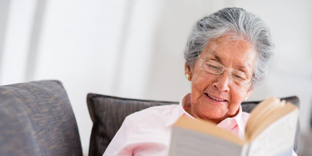Elderly woman with glasses reading a book